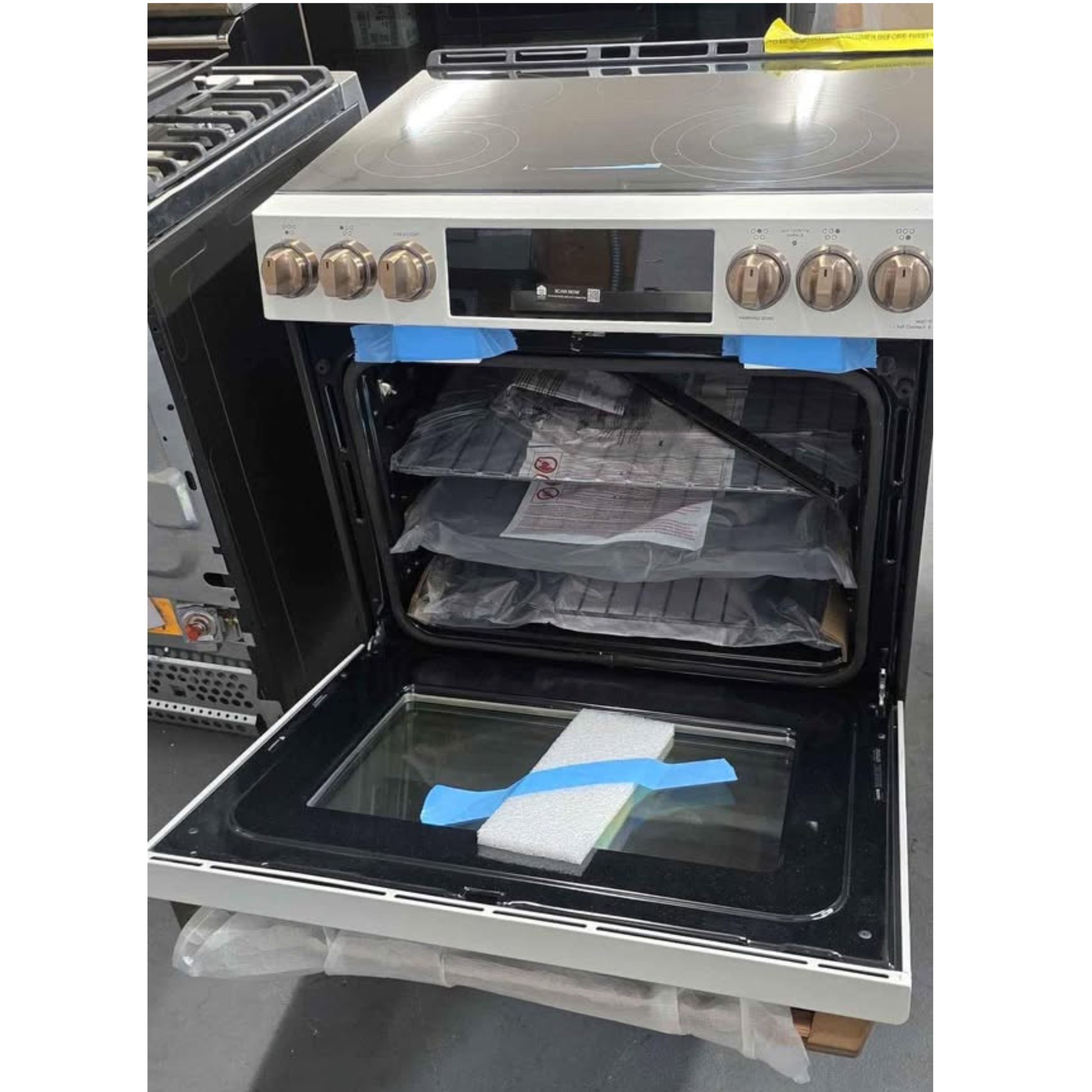 A freestanding electric range with the oven door open, showing the interior racks and glass door. The appliance has a white front, black cooktop and oven interior, and metallic control knobs.
