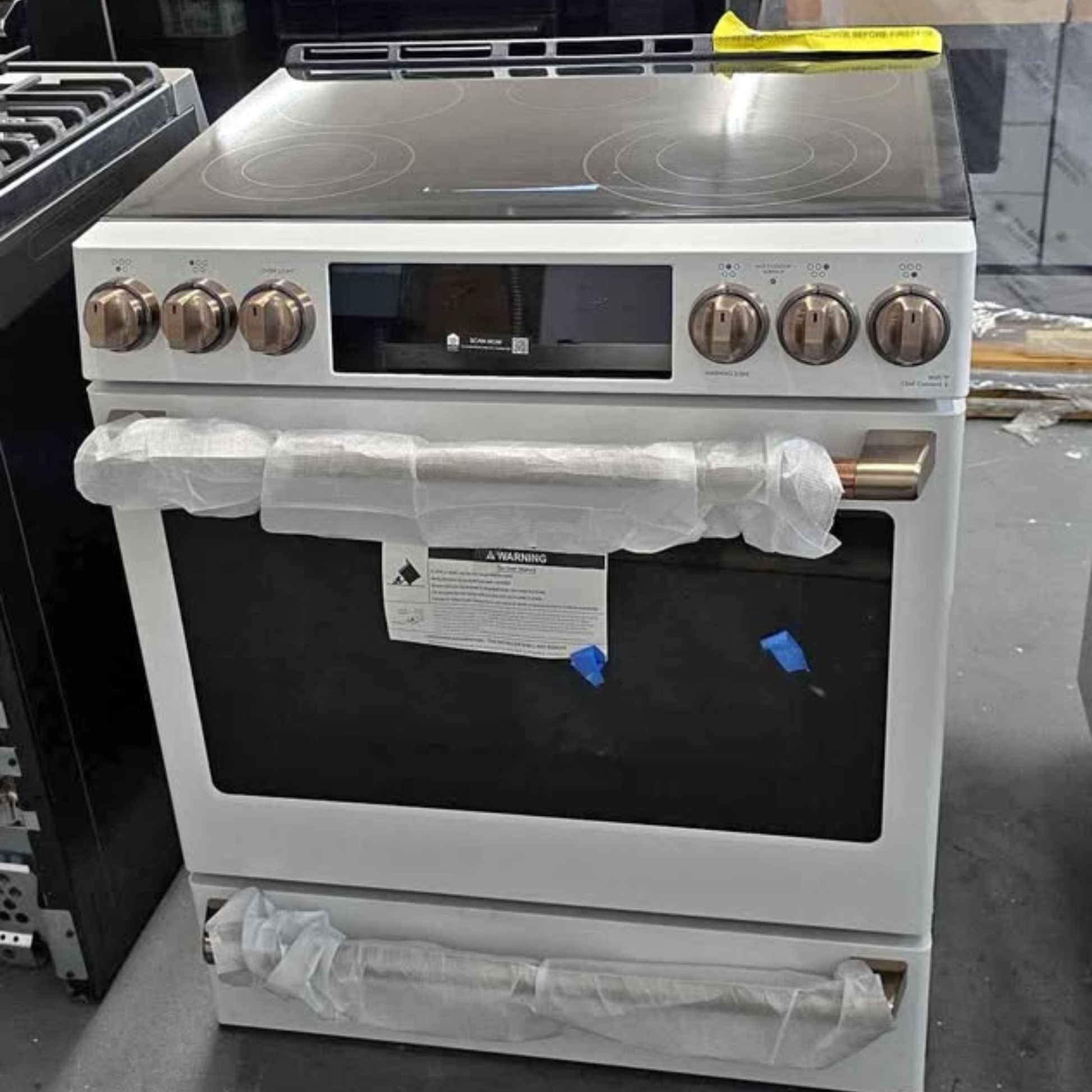 Image 1: GE Cafe matte white electric range interior view with oven racks and glass cooktop
Image 2: GE Cafe matte white smart electric range with bronze knobs, front view